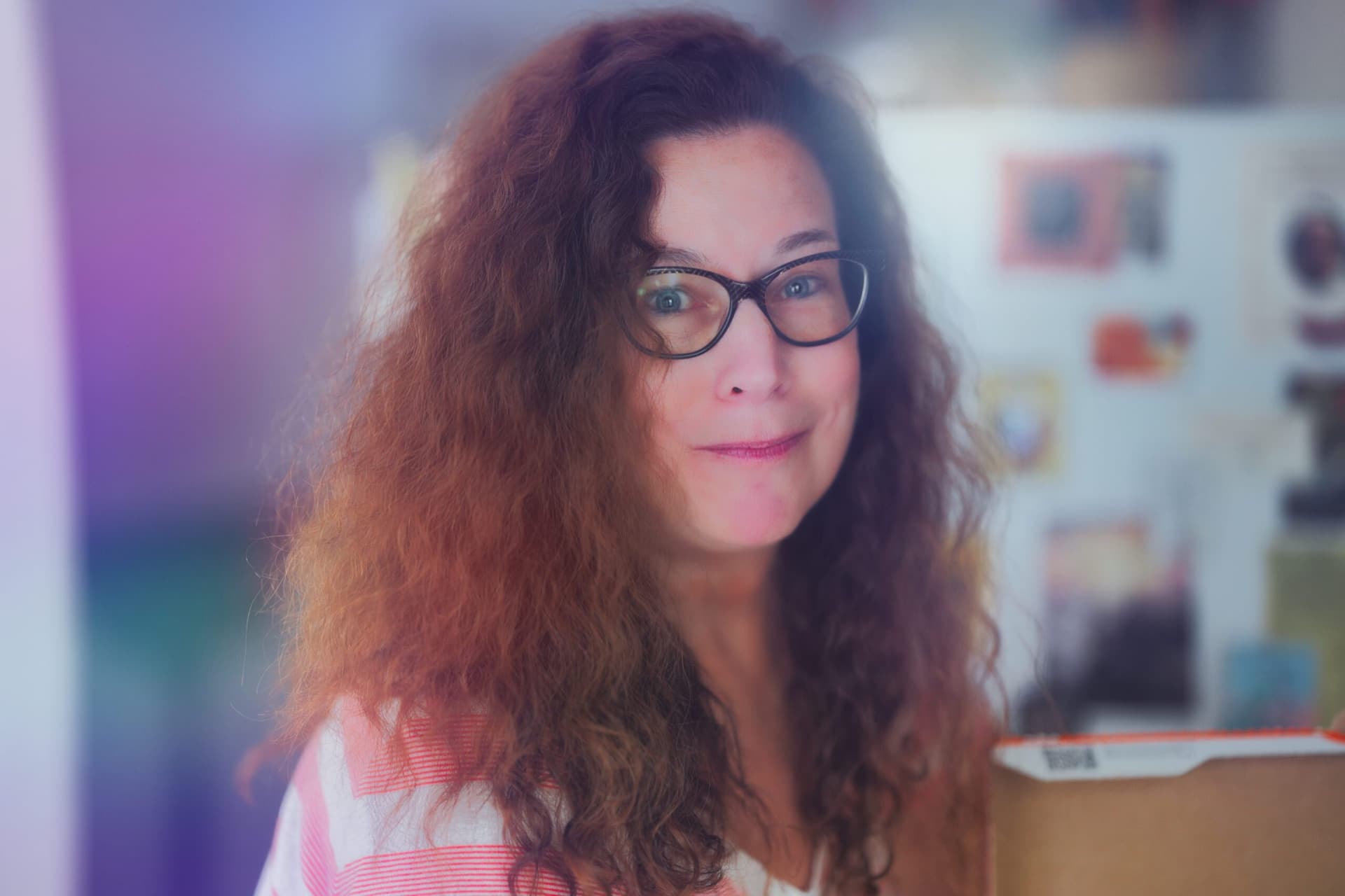 Soft-light portrait of a woman with curly hair and glasses, pastel bokeh background
