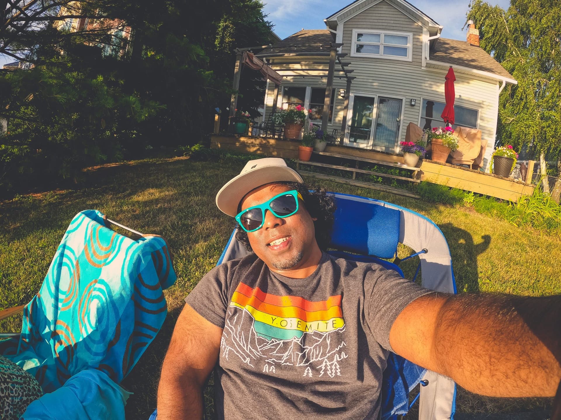 Golden-hour lawn selfie in teal sunglasses with a cottage porch in the background